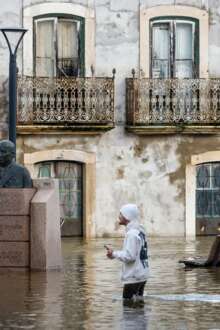 Uma estrada em Santarém inundada pela subida da Ribeira de Santarém, com uma pessoa a passar na estrada e com a água acima dos joelhos.